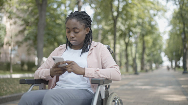 Mädchen im Rollstuhl mit Smartphone in der Hand